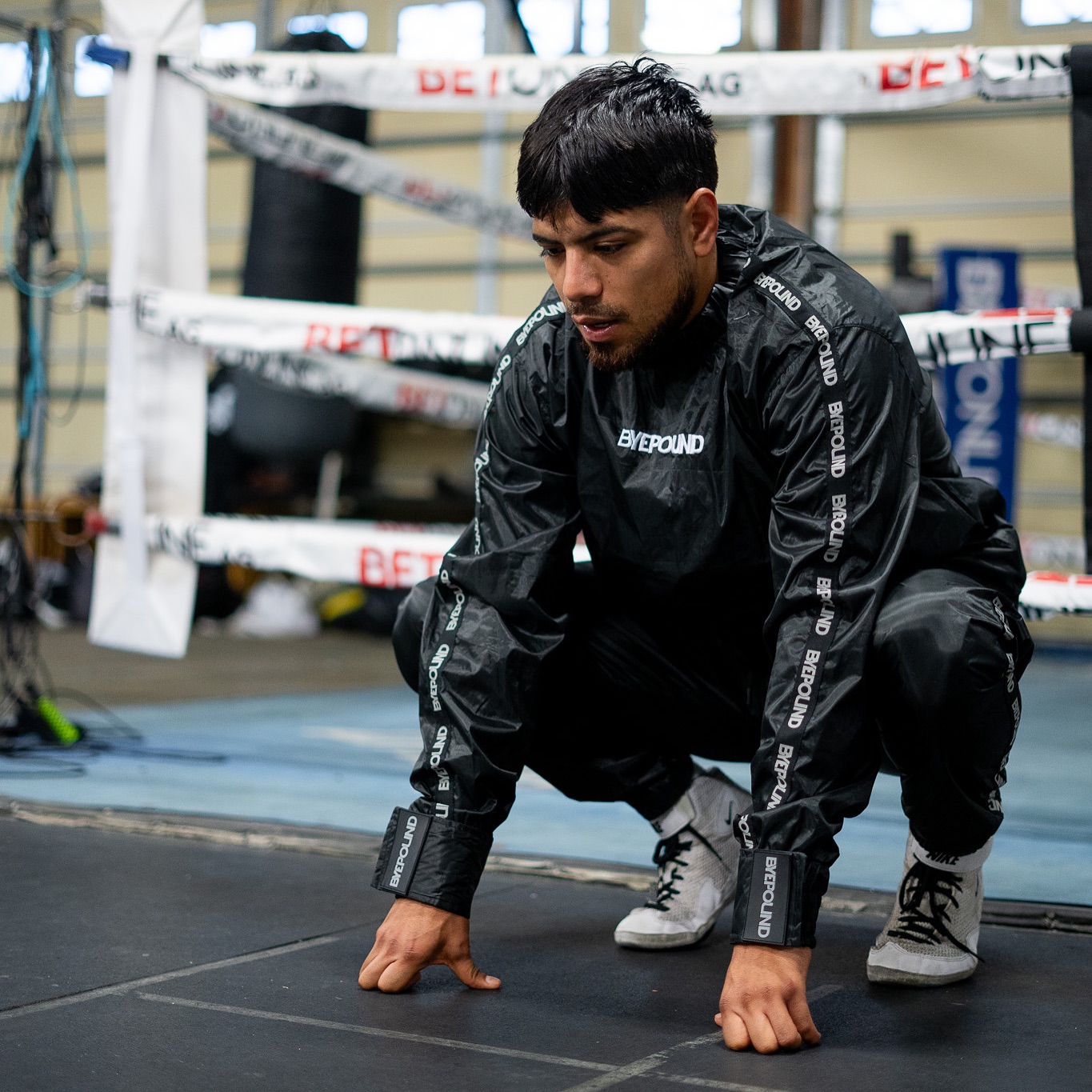 Byepound athlete squatting ringside in the signature sauna suit